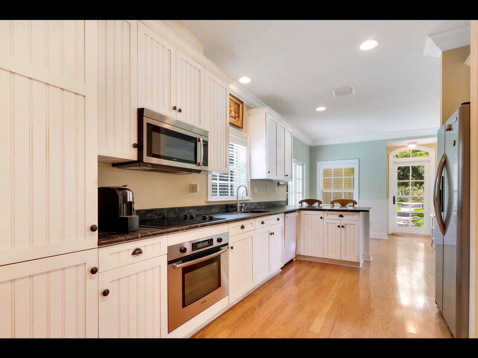 A kitchen with white beadboard cabinets, stainless steel appliances, dark countertops, and hardwood floors — 1856 SE Colony Way, Jupiter FL 33478, JUPITER, FL