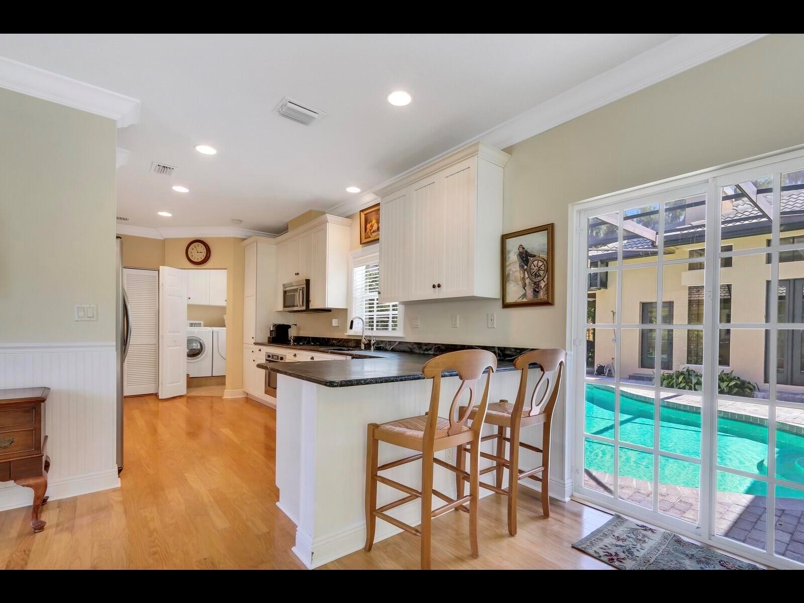 A kitchen with white cabinets, dark countertops, and a breakfast bar overlooking a swimming pool — 1856 SE Colony Way, Jupiter FL 33478, JUPITER, FL