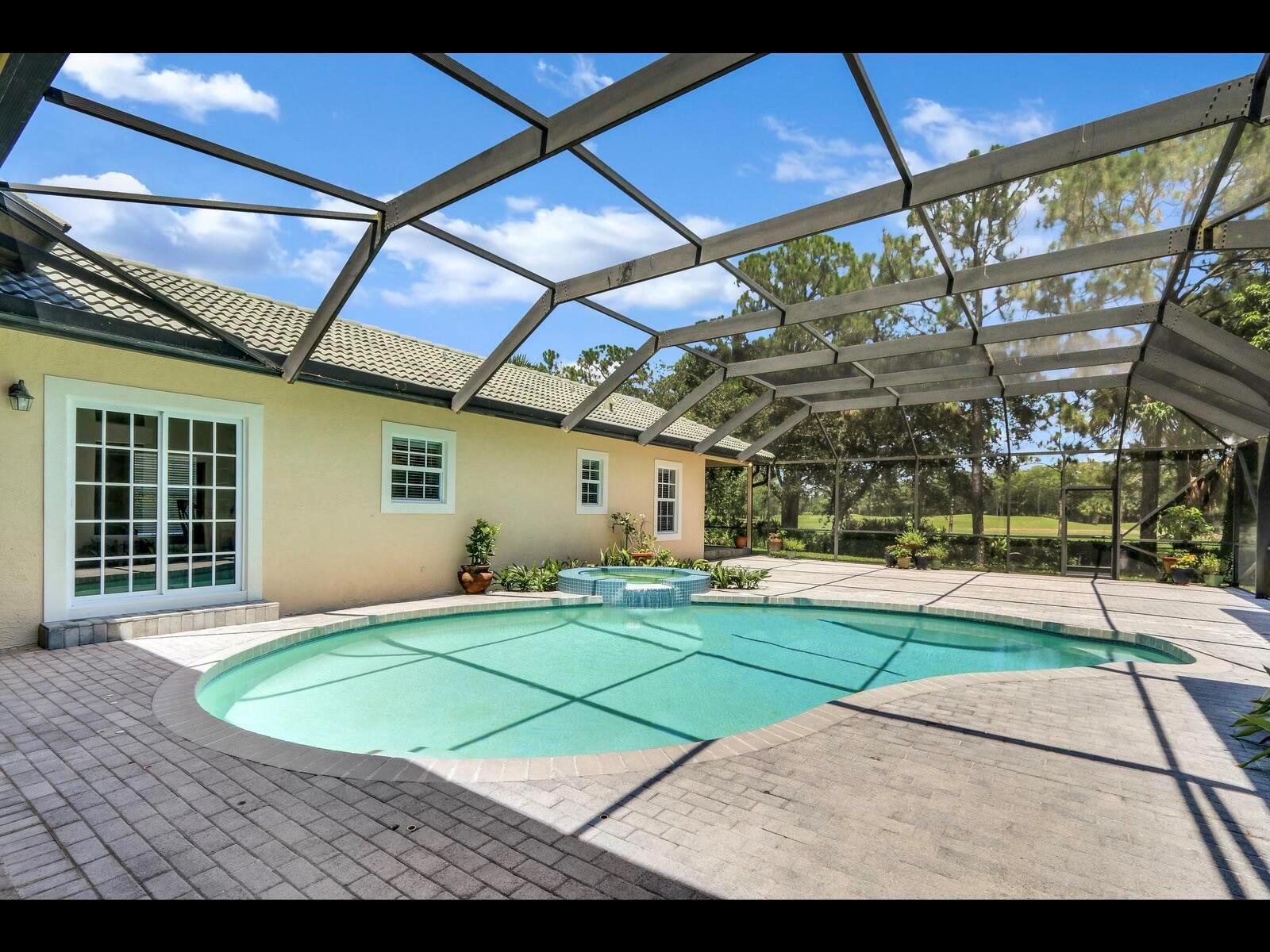 A screened-in patio features a kidney-shaped swimming pool with an attached spa and brick pavers — 1856 SE Colony Way, Jupiter FL 33478, JUPITER, FL