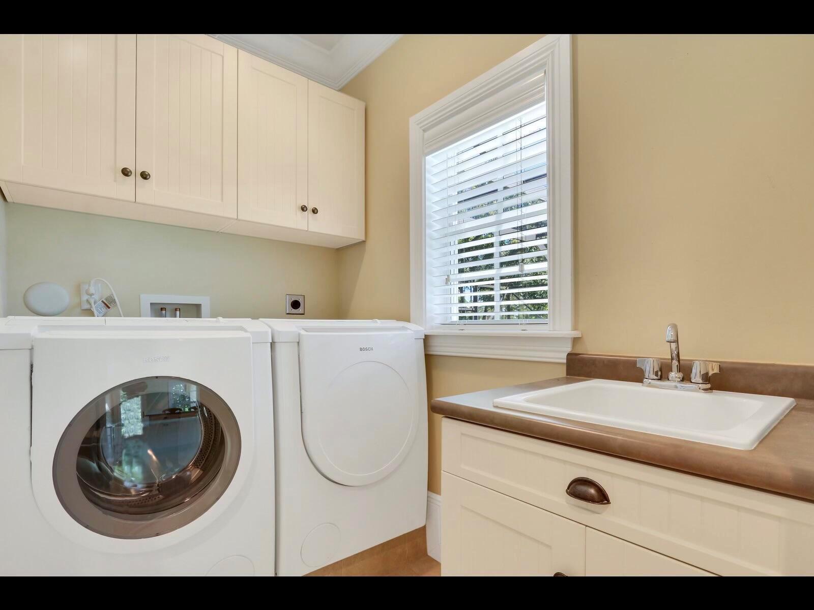 A laundry room featuring white Bosch appliances, cream cabinetry, a utility sink, and a window — 1856 SE Colony Way, Jupiter FL 33478, JUPITER, FL