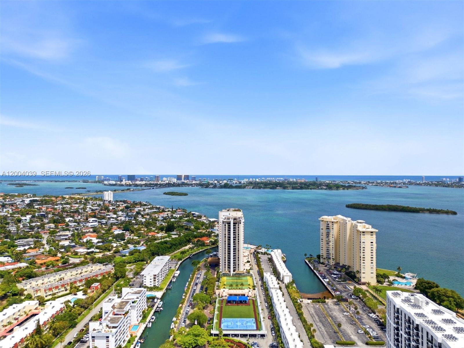 An aerial view shows high-rise buildings, a canal, and a sports court near the ocean — 1800 NE 114th St # 1505, Miami FL 33181, MIAMI, FL