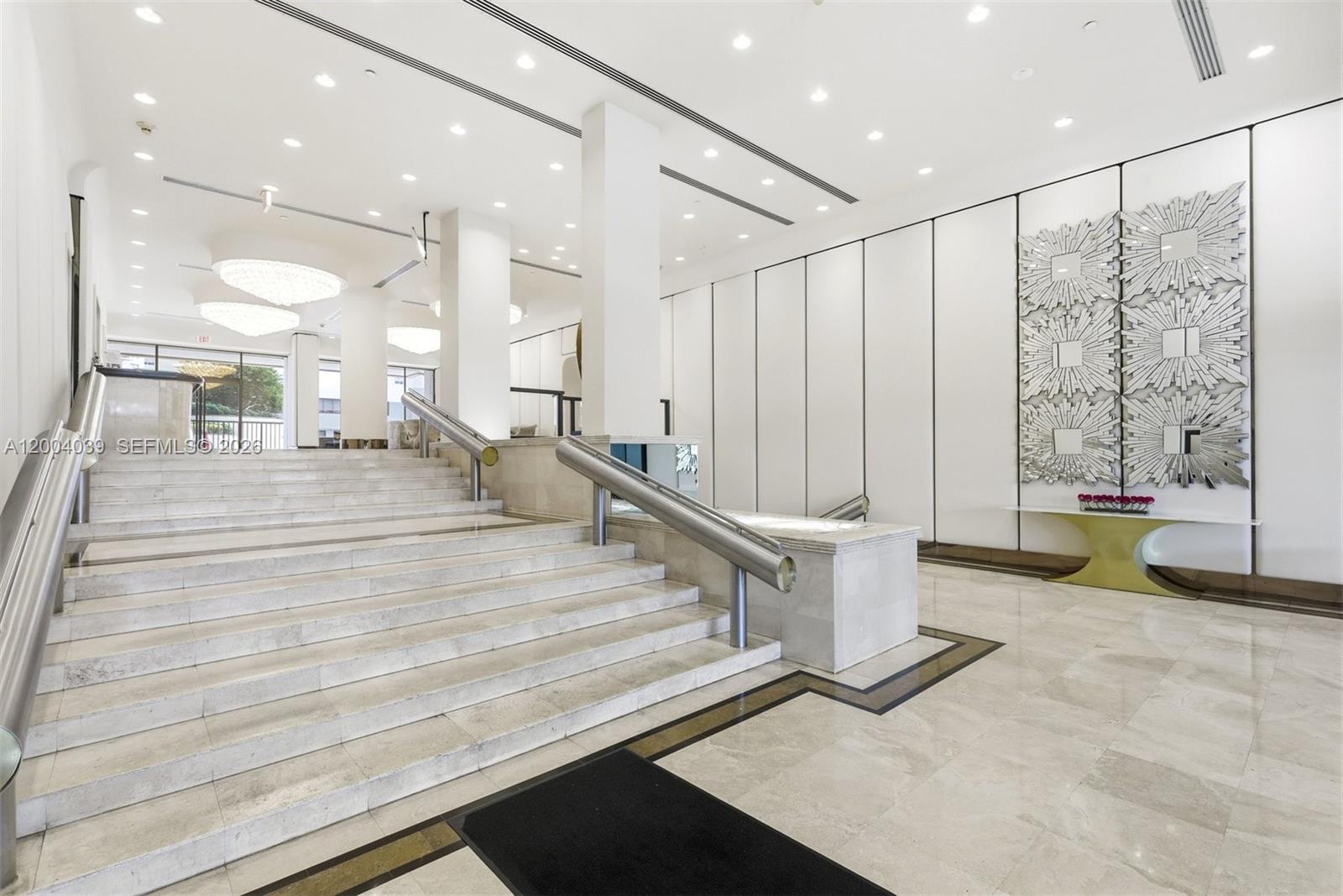 A bright, modern building lobby features a wide marble staircase with metal handrails — 1800 NE 114th St # 1505, Miami FL 33181, MIAMI, FL