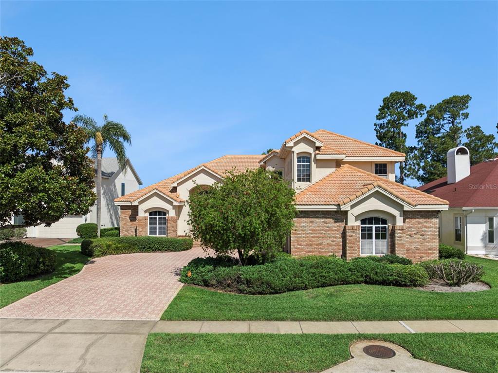 A two-story brick house with a tile roof and a paved driveway under a blue sky — 1901 EDGEWATER DRIVE, MOUNT DORA, FL
