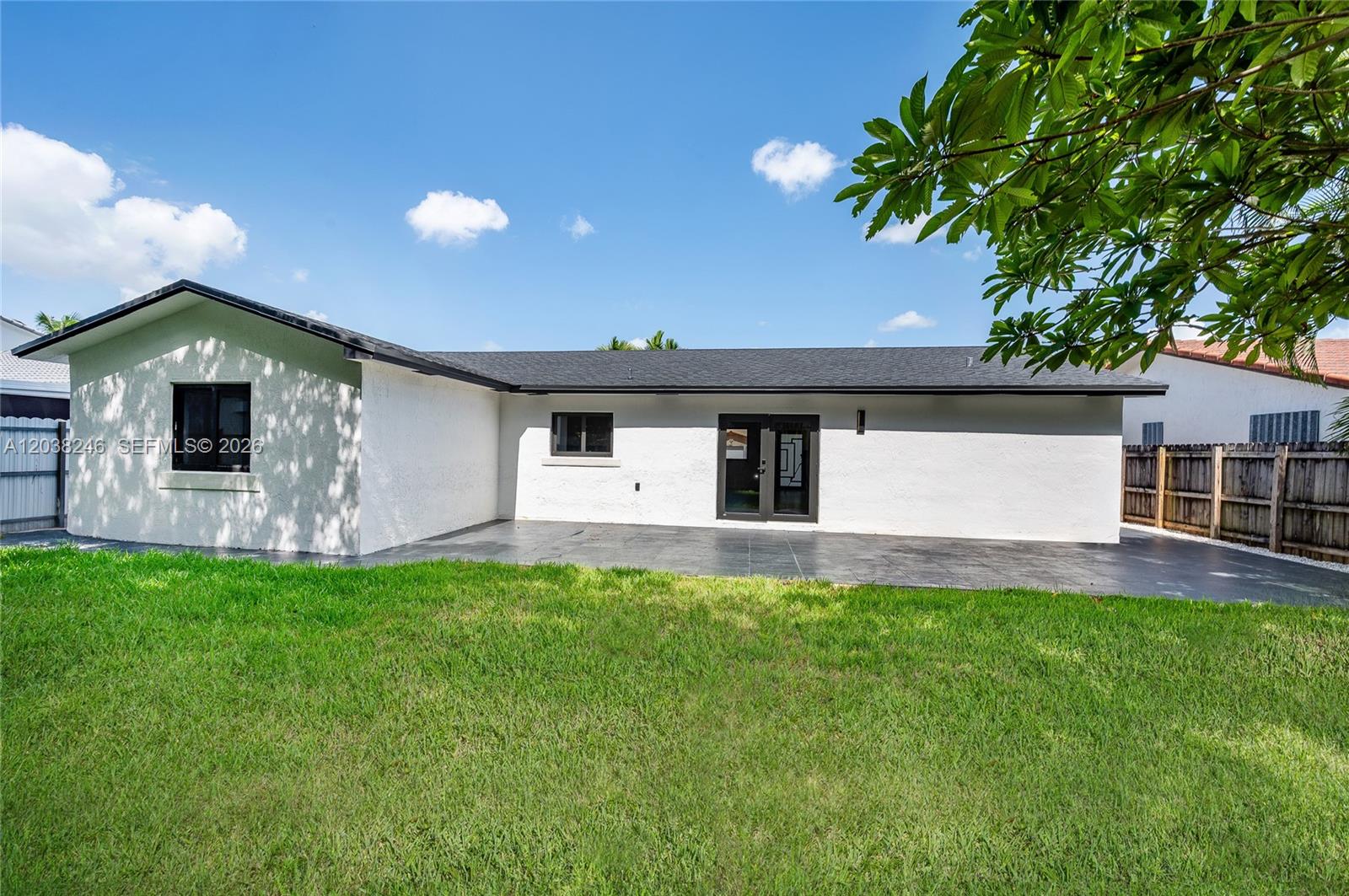 The exterior of a white house features a dark shingled roof and a paved patio — MIAMI, FL
