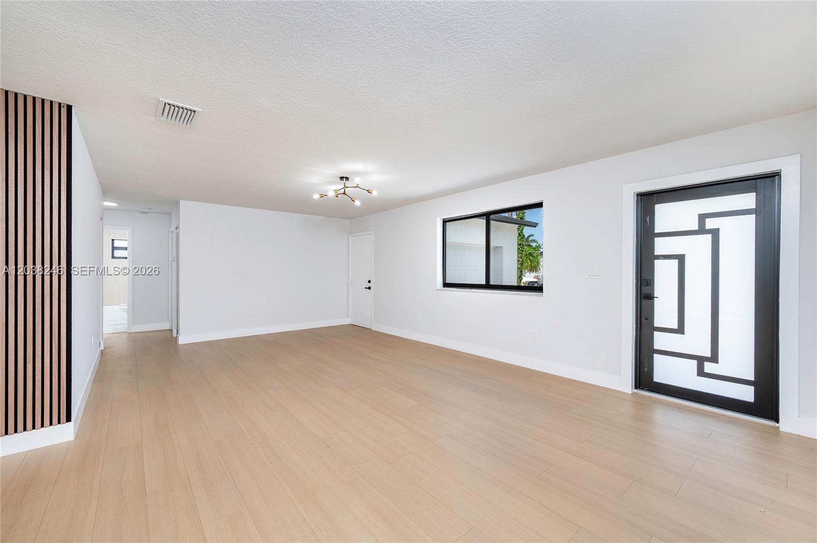 This living room features light wood flooring, white walls, a modern chandelier, and a decorative door — MIAMI, FL