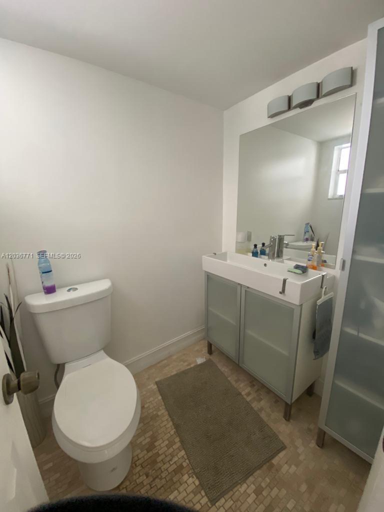 A bathroom features a white toilet, a modern vanity with a sink, and a large mirror — 873 NE 195th St # 308, Miami FL 33179, MIAMI, FL