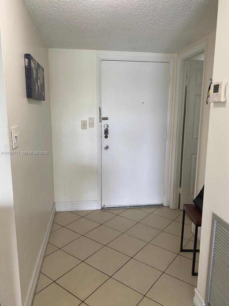 A tiled entryway features a white front door, a wall-mounted thermostat, and a small painting — 873 NE 195th St # 308, Miami FL 33179, MIAMI, FL
