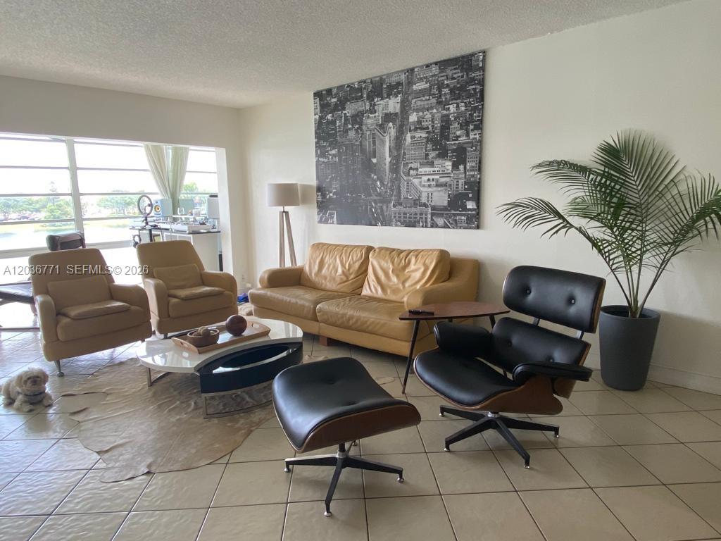 A living room features a tan sofa, a black lounge chair with ottoman, and tile flooring — 873 NE 195th St # 308, Miami FL 33179, MIAMI, FL
