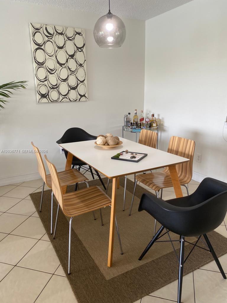 A dining room features a white table, mixed chairs, a rug, and wall art — 873 NE 195th St # 308, Miami FL 33179, MIAMI, FL