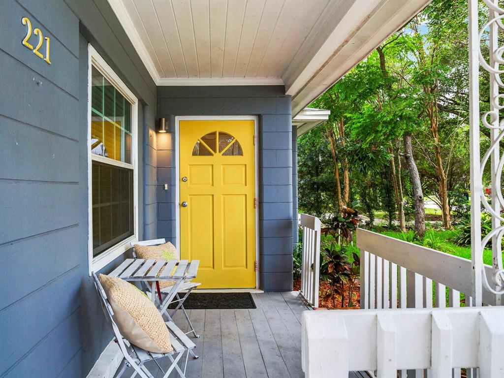 A front porch features a yellow door, gray siding, and a small bistro set — 221 N CLEARVIEW AVENUE, TAMPA, FL