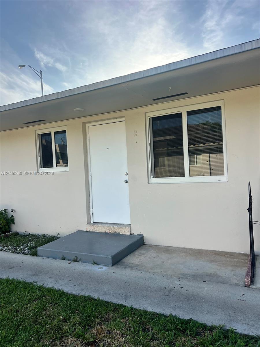The exterior of a single-story building features a white door, two windows, and a concrete stoop — HIALEAH, FL