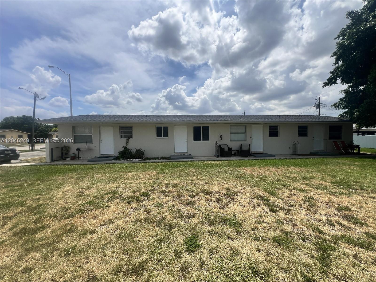 A single-story multi-unit residential building features four white doors and a large front lawn — HIALEAH, FL