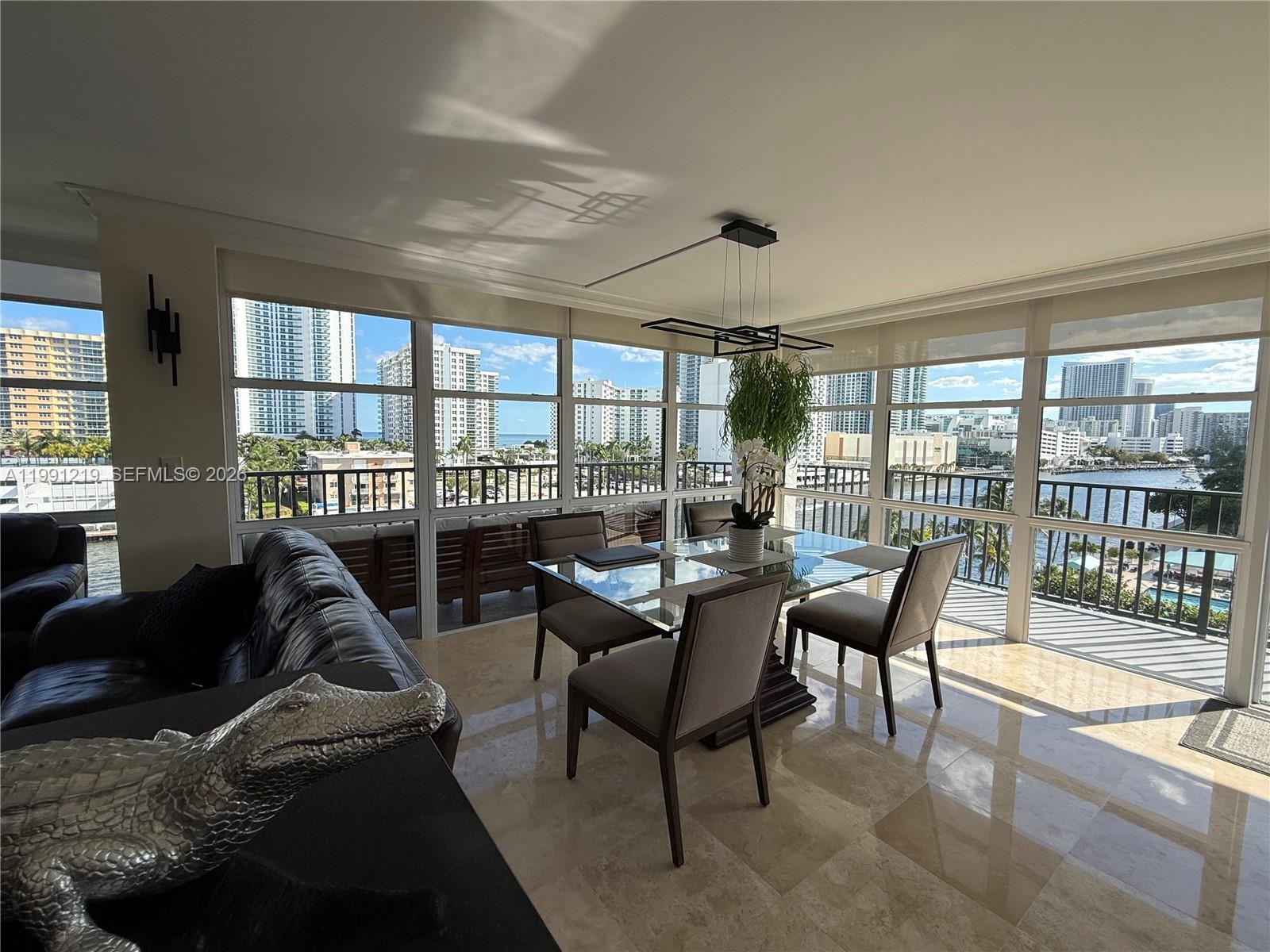 A dining area with a glass table and chairs overlooks a balcony and city skyline — 1000 Parkview Dr # 720, Hallandale Beach FL 33009, HALLANDALE BEACH, FL