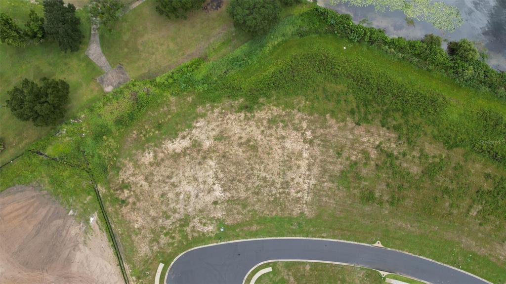 An aerial view shows a vacant, grassy residential lot situated along a curved paved road — 1105 ENCLAVE COURT, AUBURNDALE, FL