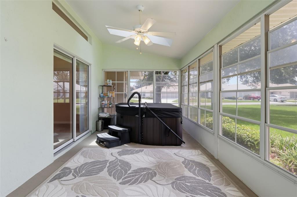 A sunroom features a hot tub, a patterned area rug, and large windows overlooking a lawn — 4646 INVERNESS DRIVE, LEESBURG, FL