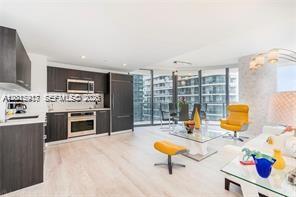 A modern open-concept kitchen and living area with dark cabinetry, light floors, and floor-to-ceiling windows — 45 SW 9th St # 1701, Miami FL 33130, MIAMI, FL