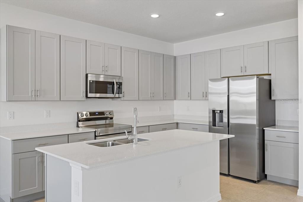 A modern kitchen features gray cabinets, stainless steel appliances, and a white quartz island countertop — 519 SILVER PALM DRIVE, HAINES CITY, FL