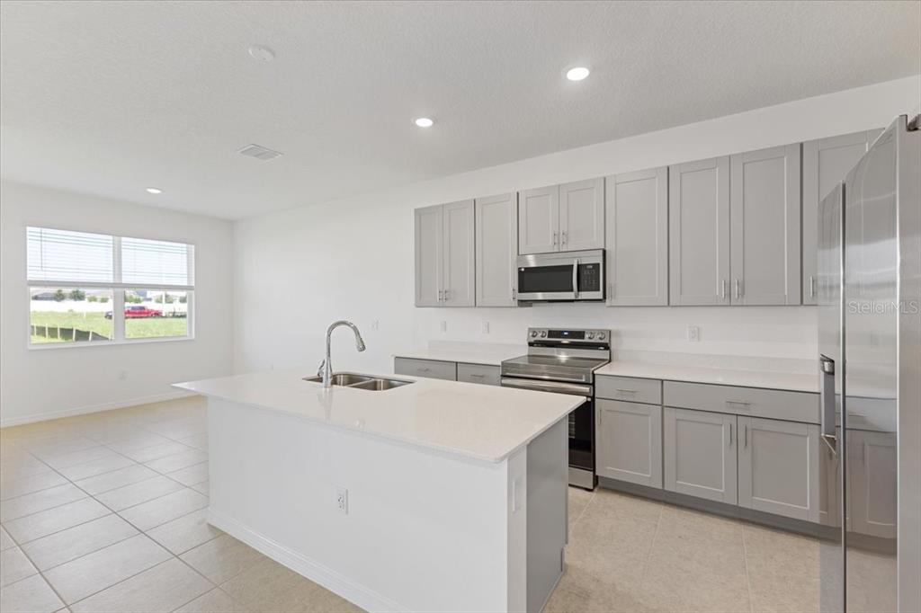 A kitchen features gray cabinets, white countertops, a center island, and stainless steel appliances — 519 SILVER PALM DRIVE, HAINES CITY, FL
