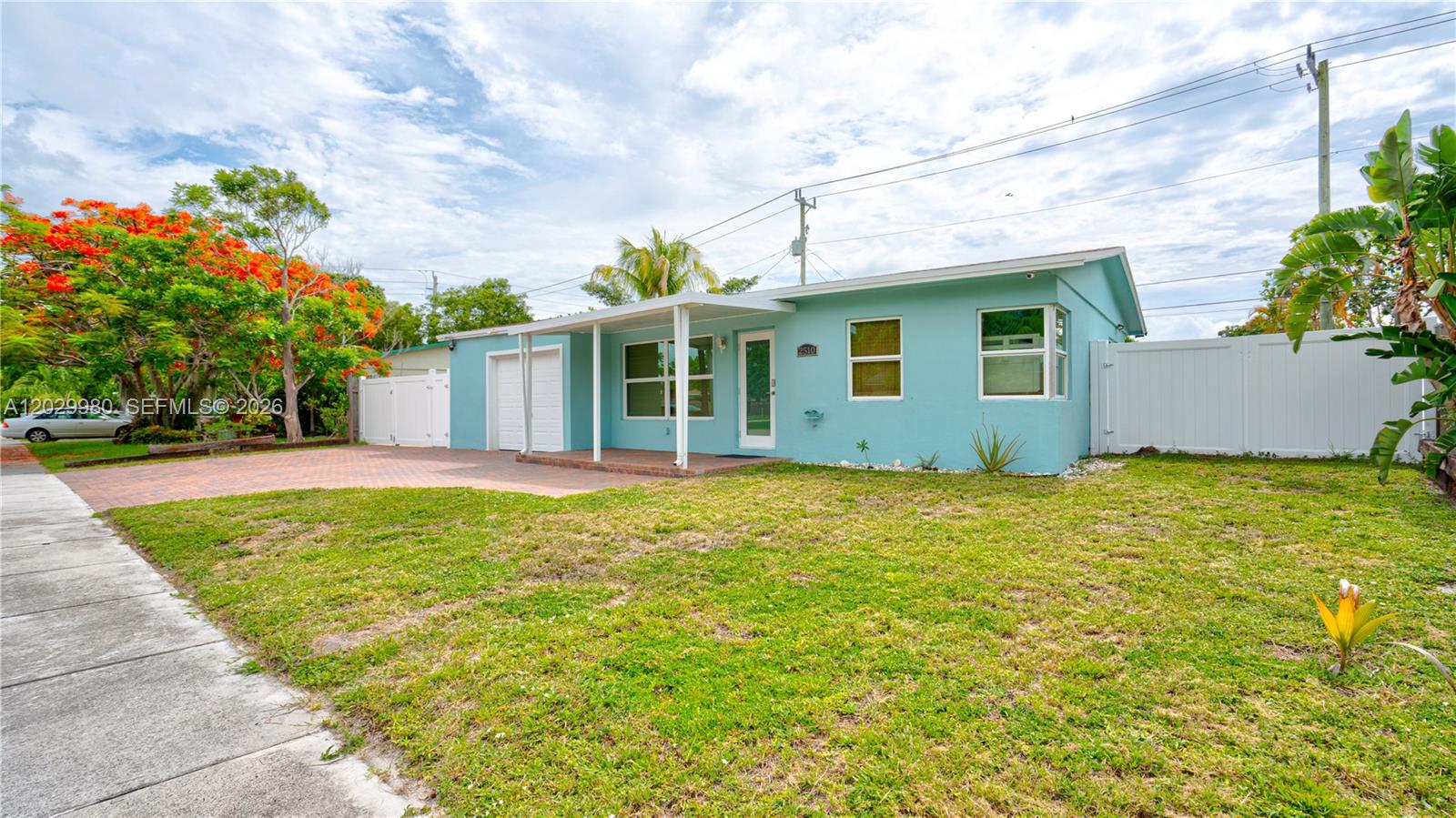 A light blue, single-story house features a covered entryway, brick driveway, and white privacy fencing — 2510 NE 9th Ave, Pompano Beach FL 33064, POMPANO BEACH, FL
