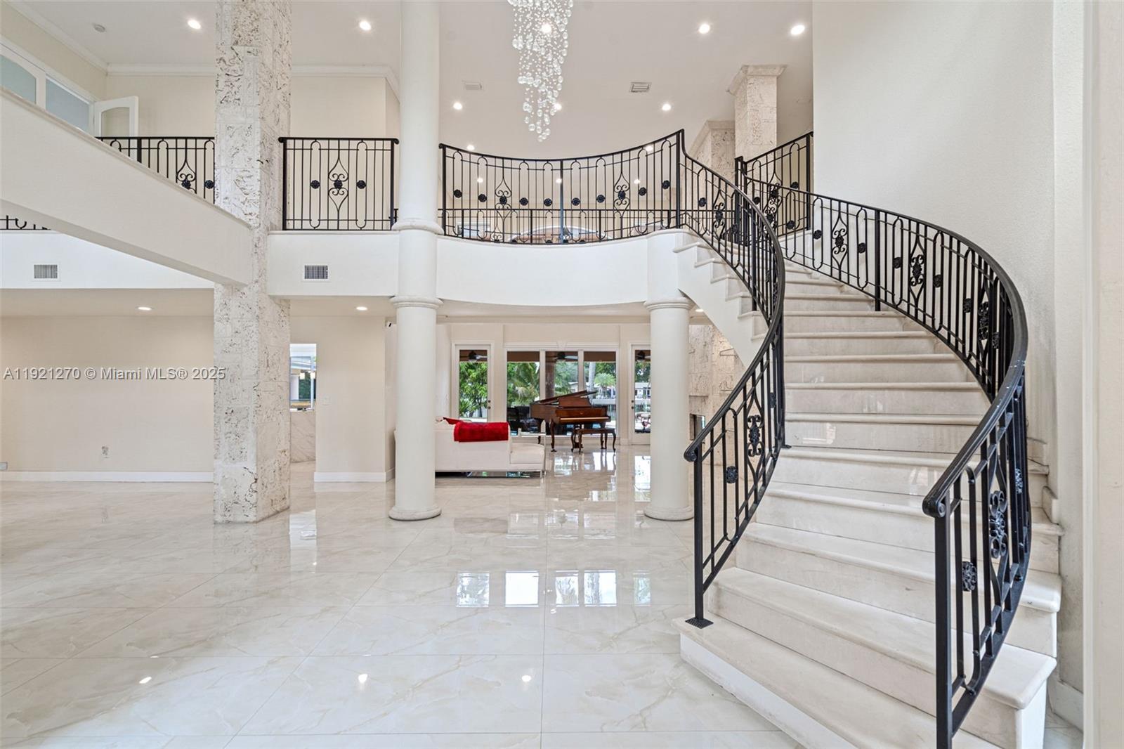 A grand foyer features a curved marble staircase, wrought iron railings, and a crystal chandelier — 7225 Gleneagle Dr, Miami Lakes FL 33014, MIAMI LAKES, FL