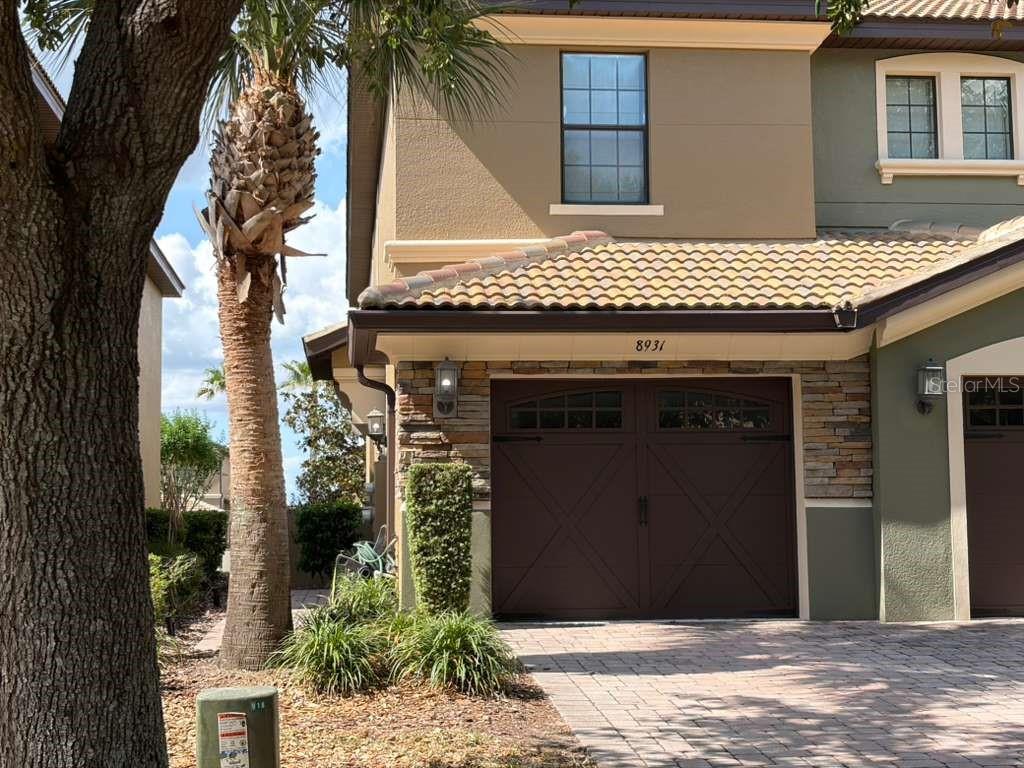 A two-story house exterior features a stone-accented garage, a palm tree, and a paved driveway — 8931 AZALEA SANDS LANE, DAVENPORT, FL