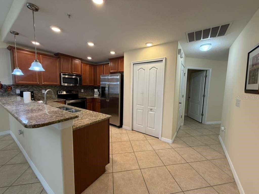 A kitchen with granite countertops, wooden cabinets, stainless steel appliances, and tile flooring — 8931 AZALEA SANDS LANE, DAVENPORT, FL