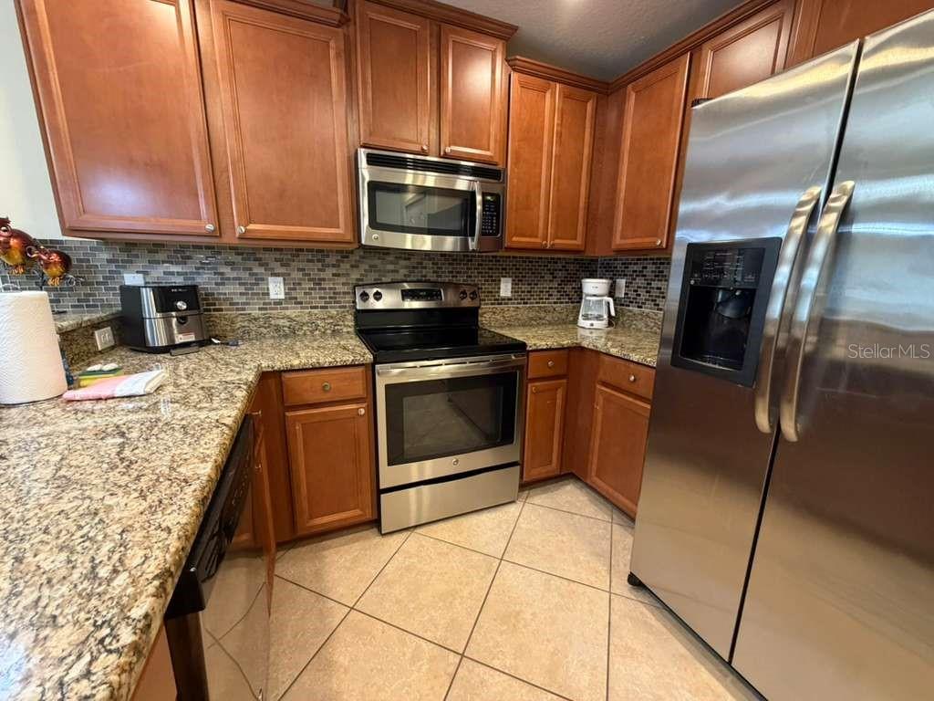 A kitchen features wood cabinets, granite countertops, stainless steel appliances, and a tiled floor — 8931 AZALEA SANDS LANE, DAVENPORT, FL