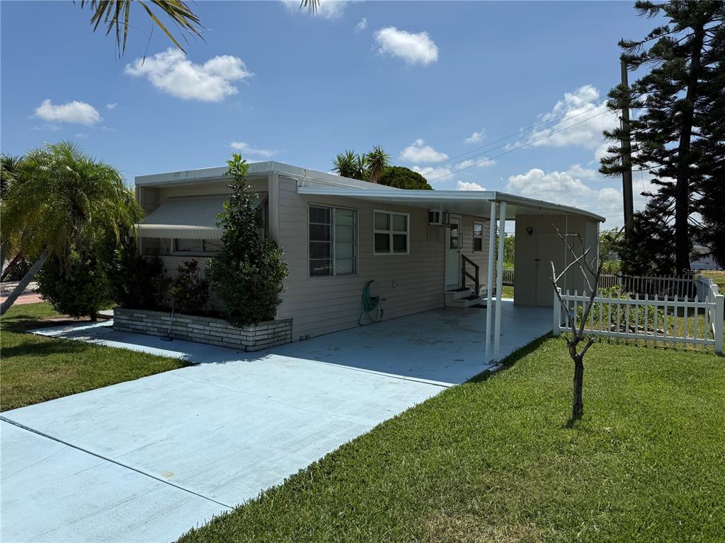 A light-colored mobile home features a carport, a concrete driveway, and a small white fence — 1508 BLIND BROOK DRIVE, SARASOTA, FL