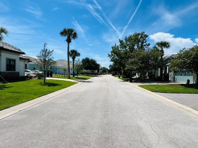 A paved residential street is lined with houses, palm trees, and green lawns under a sky — 74 LONGVIEW WAY N, PALM COAST, FL