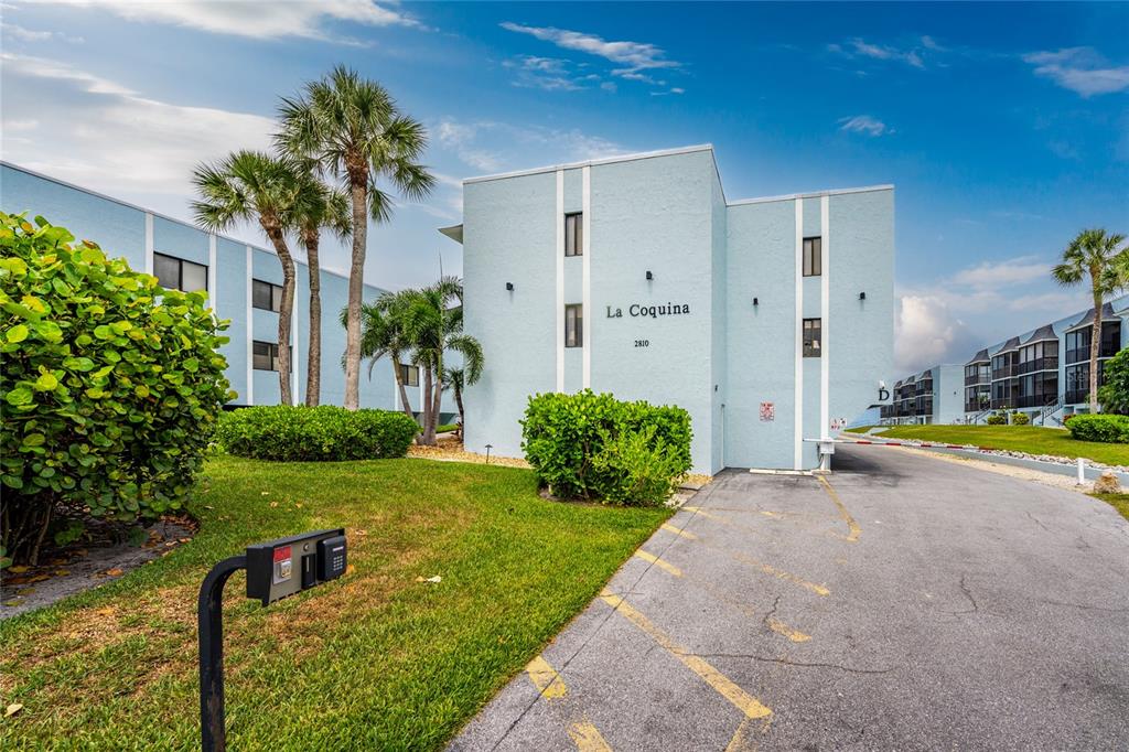 A light blue multi-story apartment building with palm trees and a gated entrance — 2810 N BEACH ROAD UNIT 108, ENGLEWOOD, FL