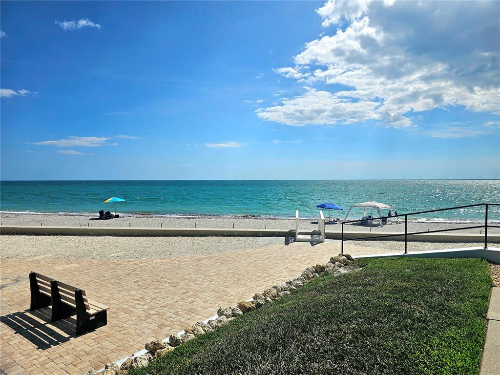 A paved patio with a bench overlooks a beach with umbrellas and the ocean — 2810 N BEACH ROAD UNIT 108, ENGLEWOOD, FL