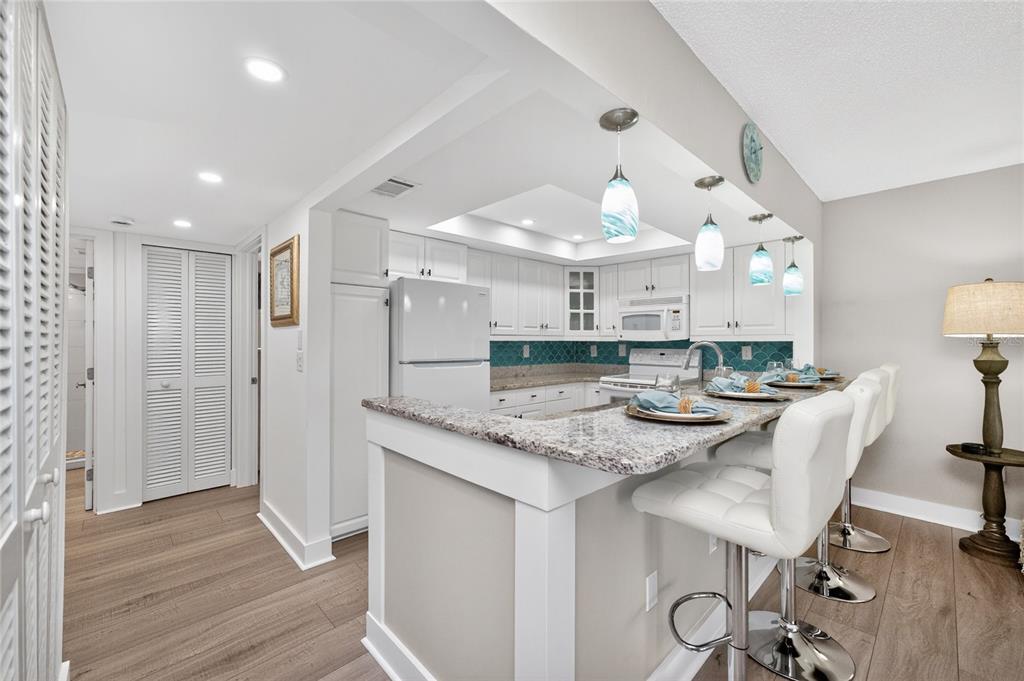 A kitchen with white cabinets, granite countertops, a teal backsplash, and a breakfast bar — 2810 N BEACH ROAD UNIT 108, ENGLEWOOD, FL