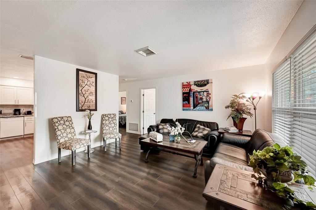 A living room with dark wood-look flooring, a black leather sofa, and two patterned chairs — 618 S OSPREY AVENUE, SARASOTA, FL