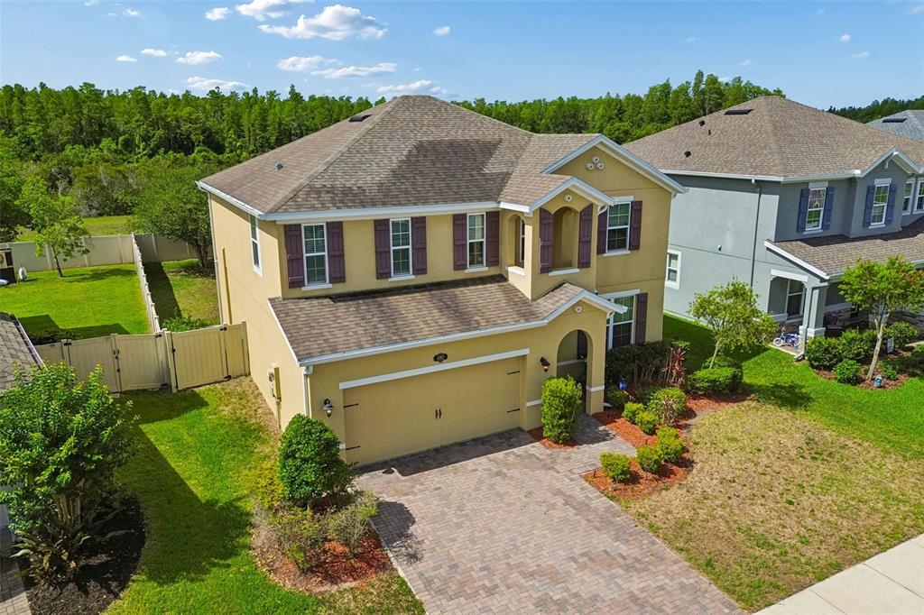 An aerial view of a two-story yellow house with a paved driveway and fenced yard — 1192 MULTIFLORA LOOP, LUTZ, FL