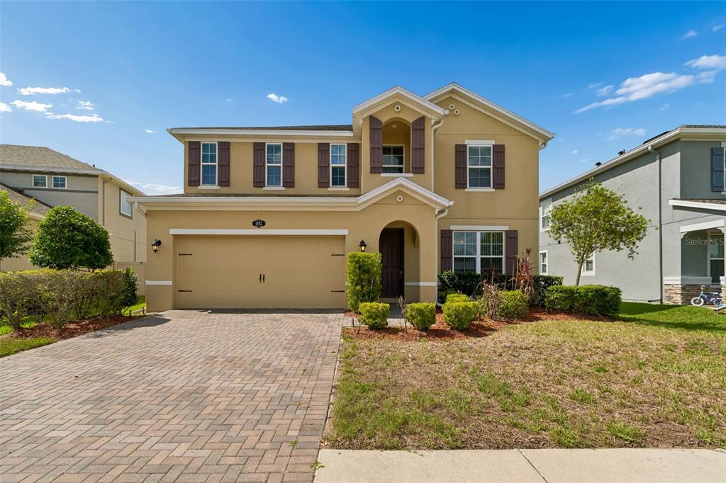 A two-story suburban house with a tan stucco exterior, brown shutters, and a paved driveway — 1192 MULTIFLORA LOOP, LUTZ, FL