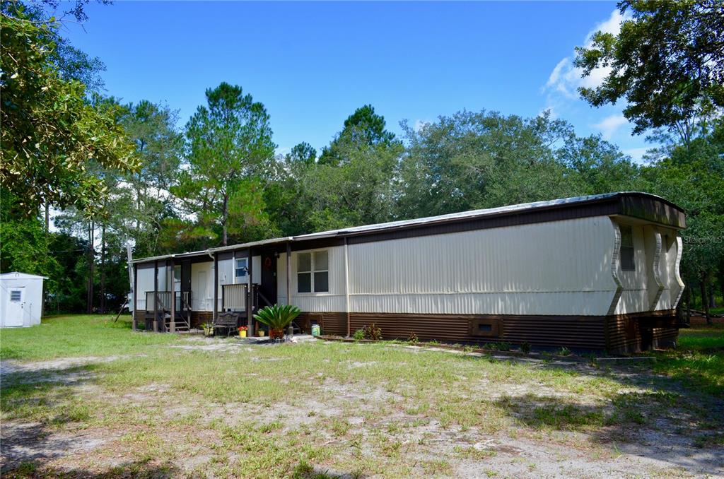 A single-wide mobile home with a metal roof and brown skirting sits on a lot — 33135 FOREST RIDGE ROAD, DELAND, FL