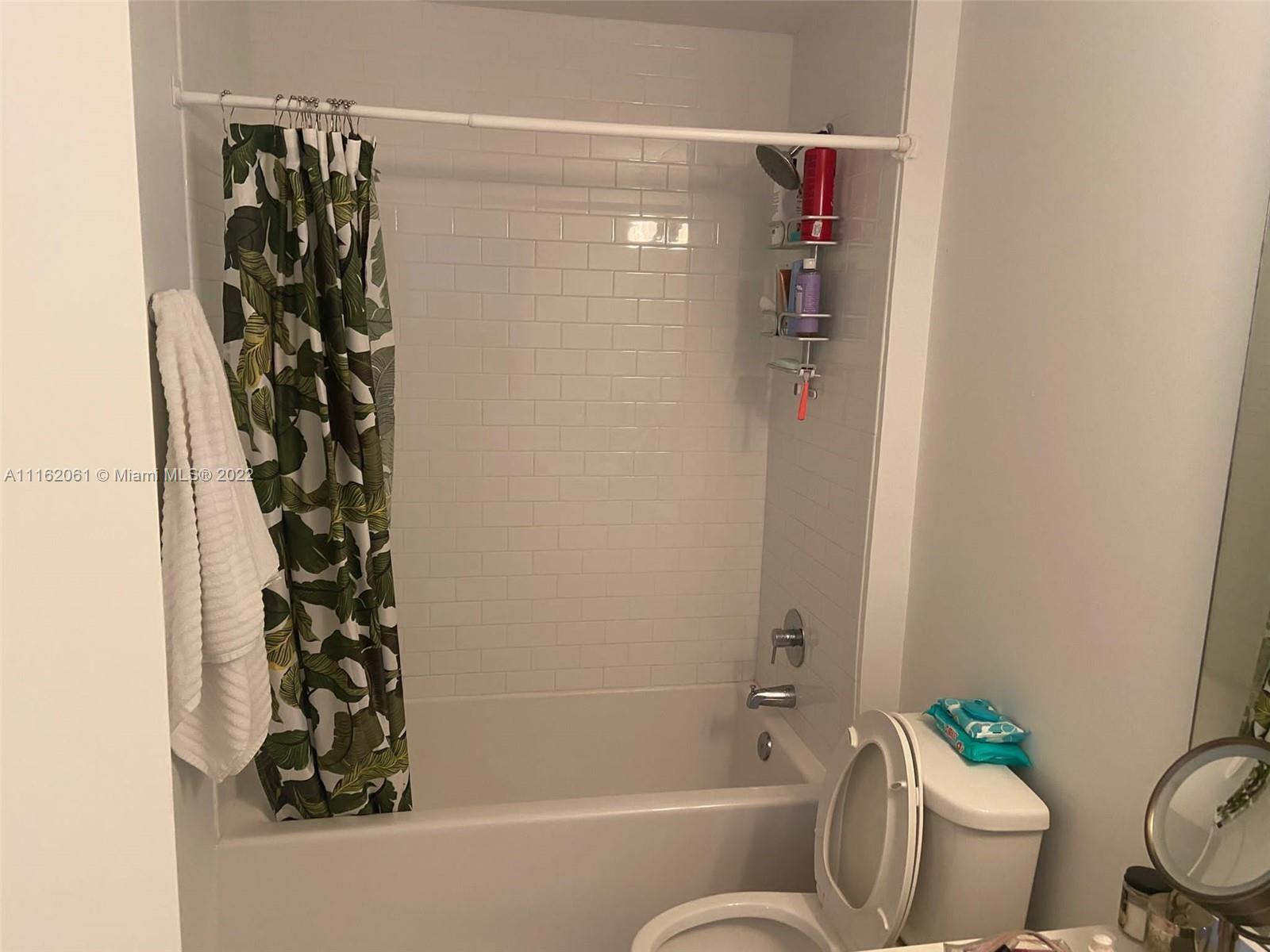A bathroom features a white subway-tiled shower area with a patterned curtain and a toilet — 151 SE 1st St, Miami FL 33131, MIAMI, FL