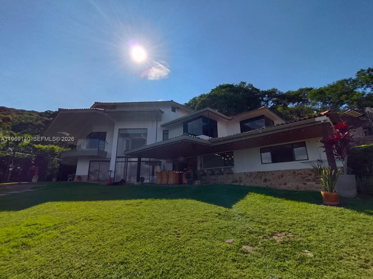 A two-story house with a large lawn, covered patio, and glass windows under a sunny sky — Via Dapa Km1, Co 760001, Co