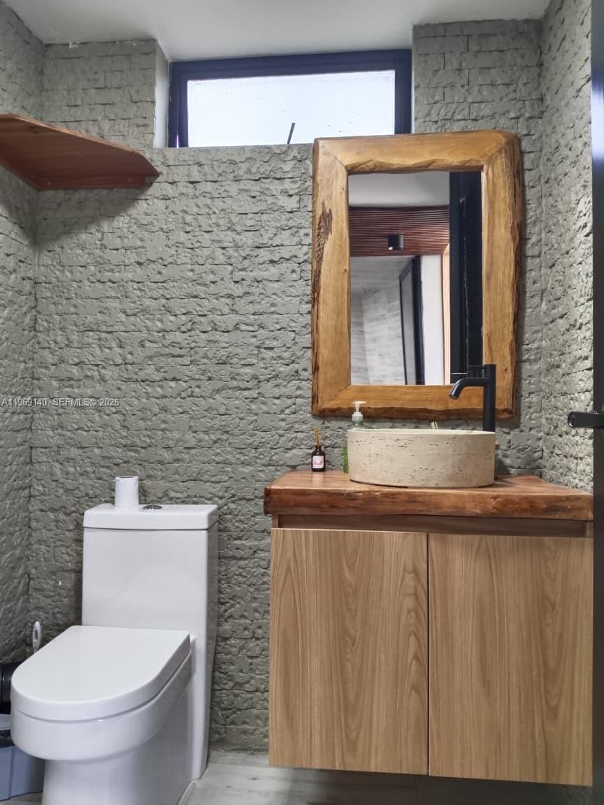 A bathroom features a stone-textured wall, a wooden vanity with a vessel sink, and a mirror — Via Dapa Km1, Co 760001, Co