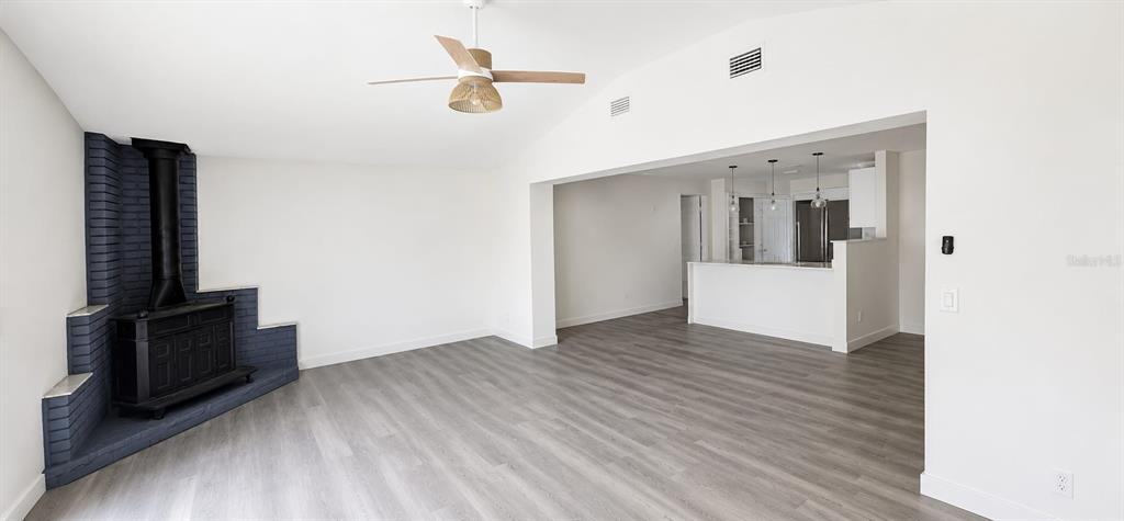 A living room with a dark brick corner fireplace and wood-look flooring leads to a kitchen — 1080 LANDERS STREET, ORMOND BEACH, FL