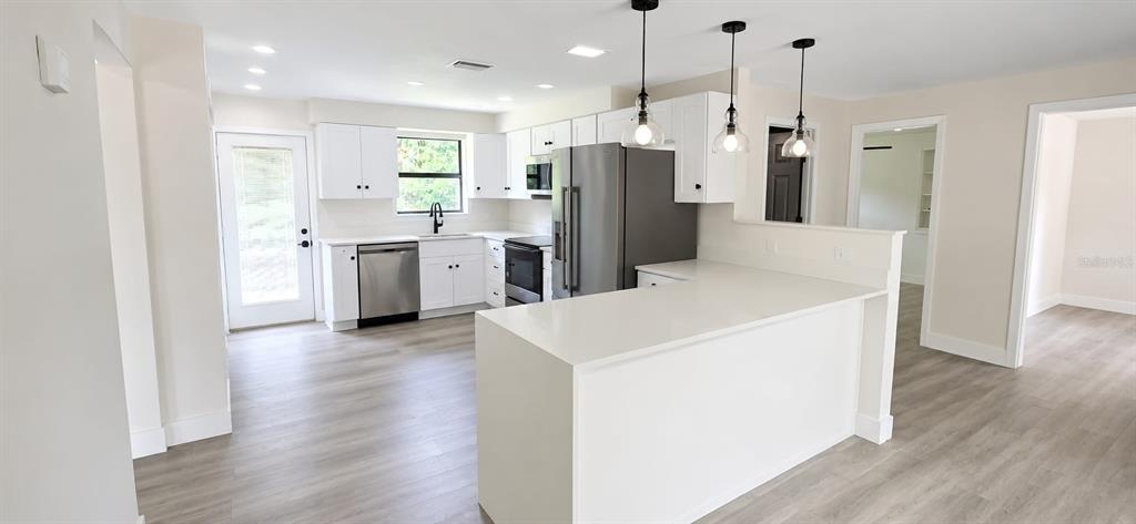 A kitchen with white cabinets, stainless steel appliances, and a quartz-topped peninsula island — 1080 LANDERS STREET, ORMOND BEACH, FL