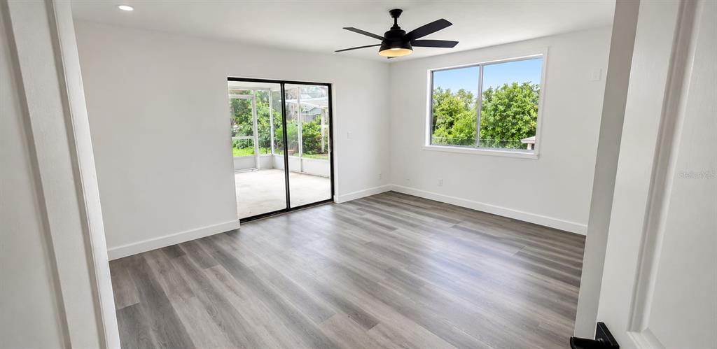A bright, empty bedroom features light gray wood-look flooring, a ceiling fan, and sliding glass doors — 1080 LANDERS STREET, ORMOND BEACH, FL