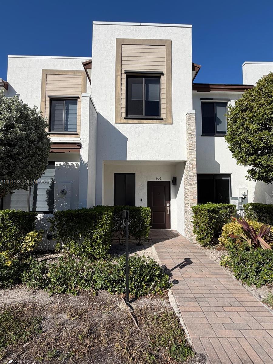 A two-story townhouse exterior features white stucco walls, brown trim, and a brick walkway — 909 NE 211th St, Miami FL 33179, MIAMI, FL