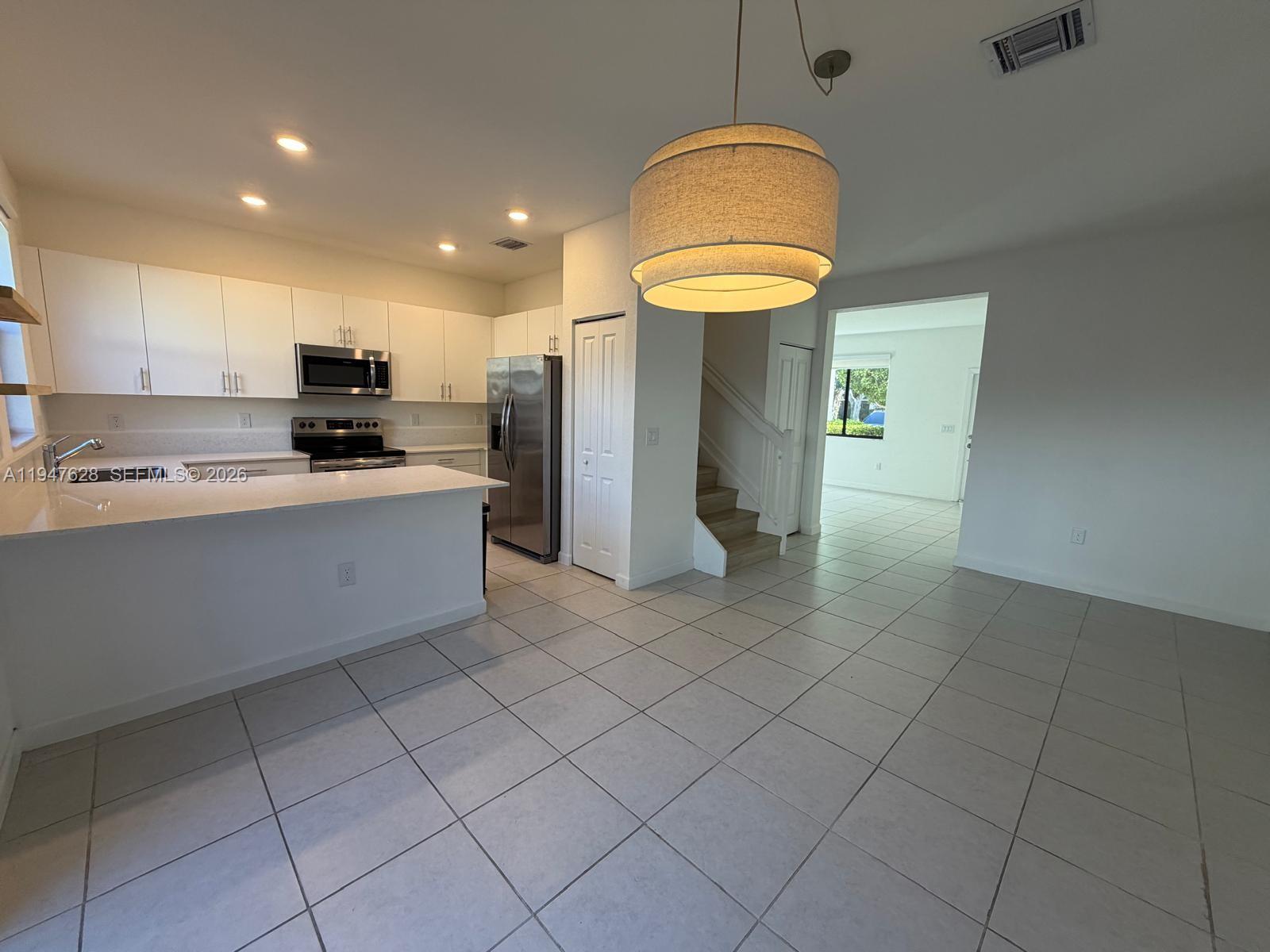 A kitchen with white cabinets, stainless steel appliances, and a large pendant light fixture — 909 NE 211th St, Miami FL 33179, MIAMI, FL