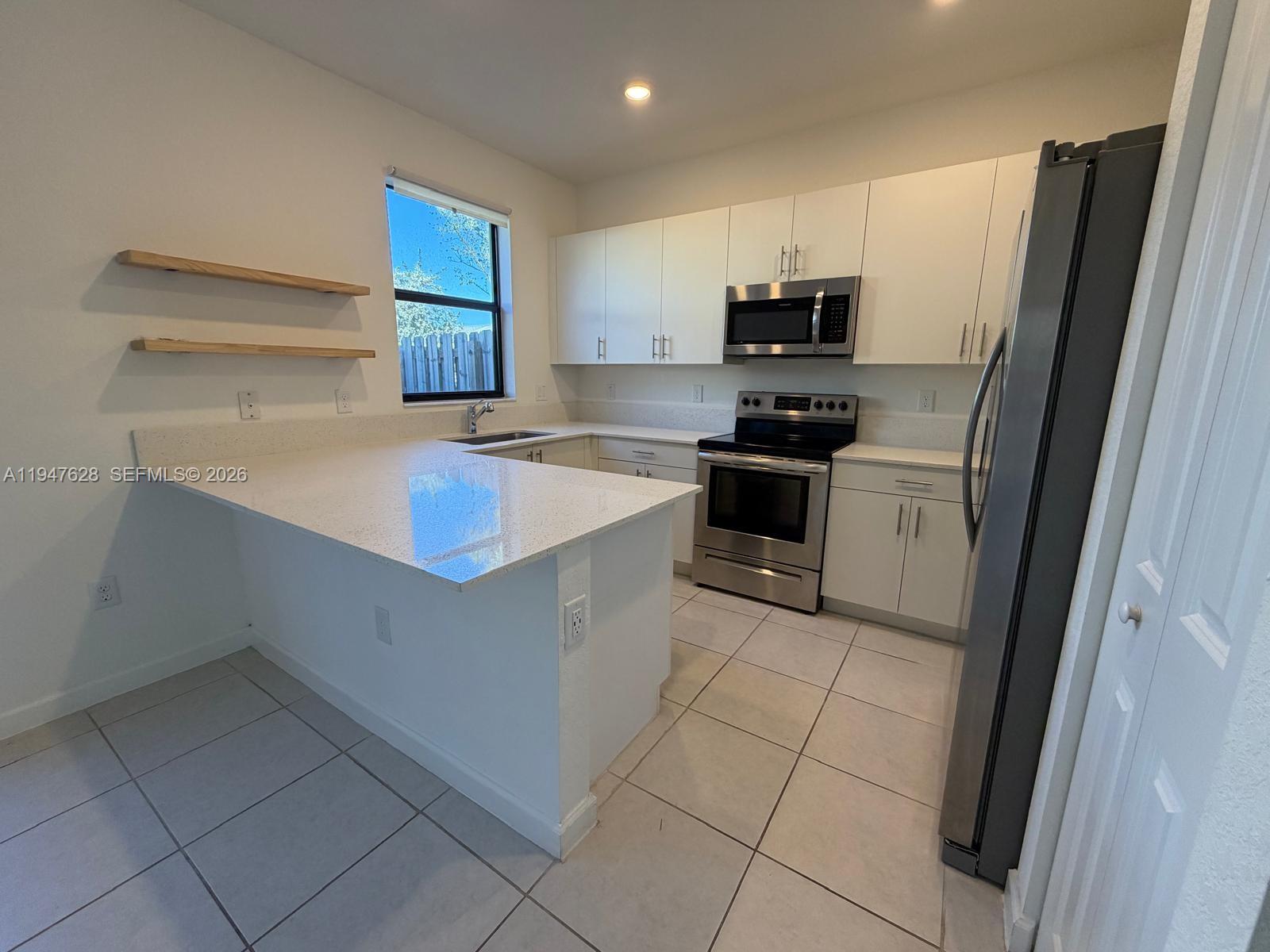 A kitchen features white cabinets, stainless steel appliances, quartz countertops, and two floating wall shelves — 909 NE 211th St, Miami FL 33179, MIAMI, FL