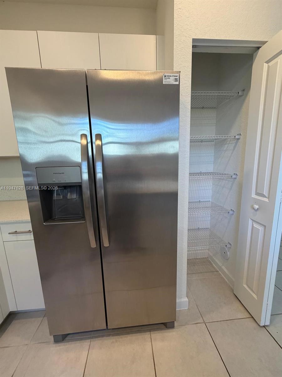 A stainless steel side-by-side refrigerator stands next to an open pantry with wire shelving — 909 NE 211th St, Miami FL 33179, MIAMI, FL
