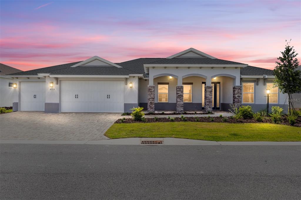 A single-story house with a three-car garage, stone-accented columns, and a paved driveway at sunset — 8512 SW 101ST AVENUE, OCALA, FL