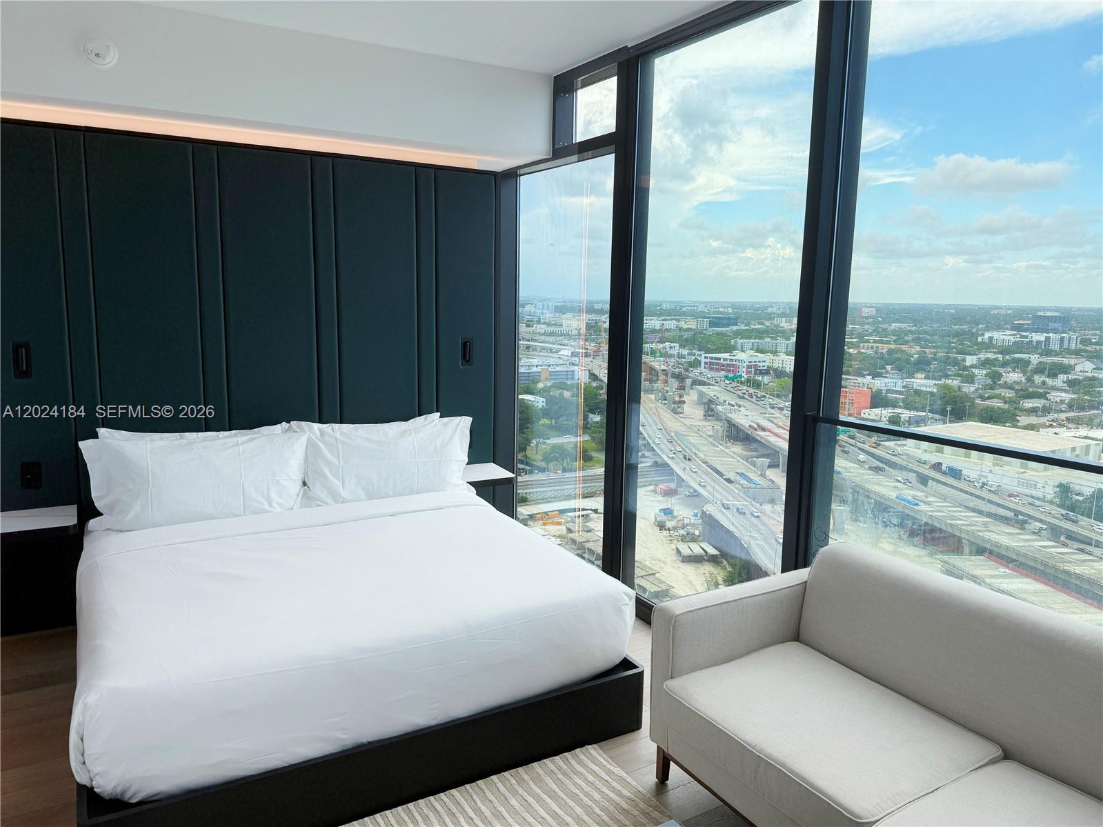 A modern bedroom features a dark paneled headboard, a white bed, and floor-to-ceiling windows — 20 NE 11 St # 2601, Miami FL 33132, MIAMI, FL
