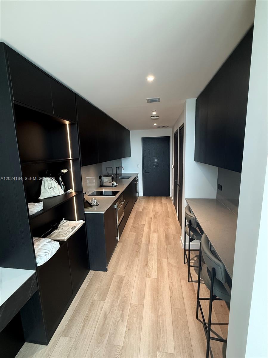 A galley kitchen features black cabinetry, light wood flooring, and a built-in breakfast bar — 20 NE 11 St # 2601, Miami FL 33132, MIAMI, FL