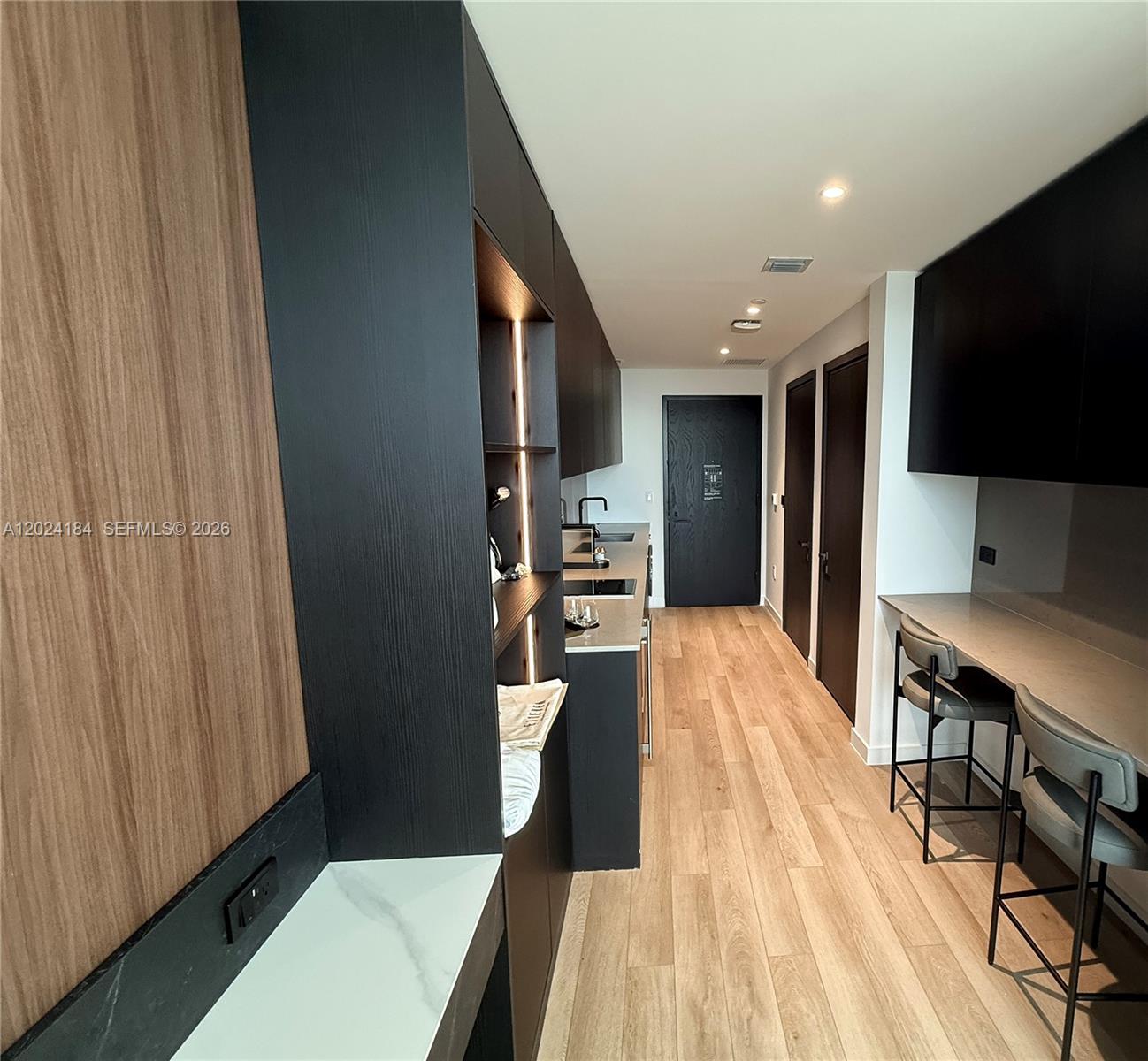 A narrow kitchen features dark cabinetry, light wood flooring, and a built-in breakfast bar — 20 NE 11 St # 2601, Miami FL 33132, MIAMI, FL